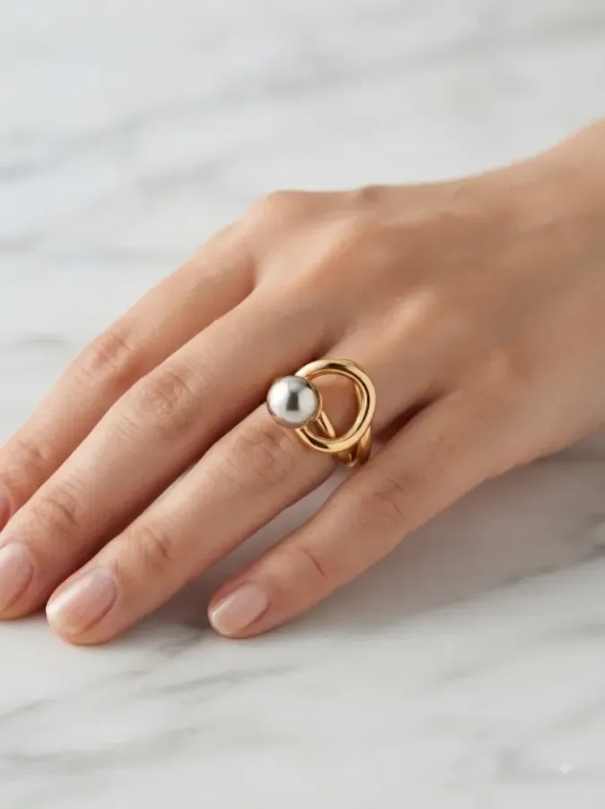 Bague bicolore dorée avec perle sphérique argentée portée à la main