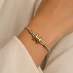 Bracelet cordon blanc et motif lettre H doré porté au poignet