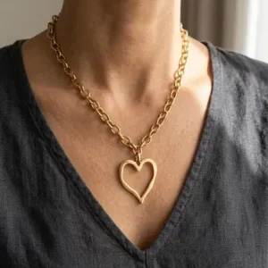 Collier doré à grosse chaîne et pendentif grand cœur ajouré porté au décolleté