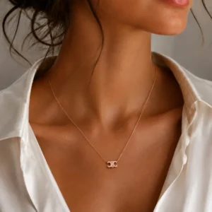Collier pendentif double C doré porté délicatement au décolleté sur chemisier blanc